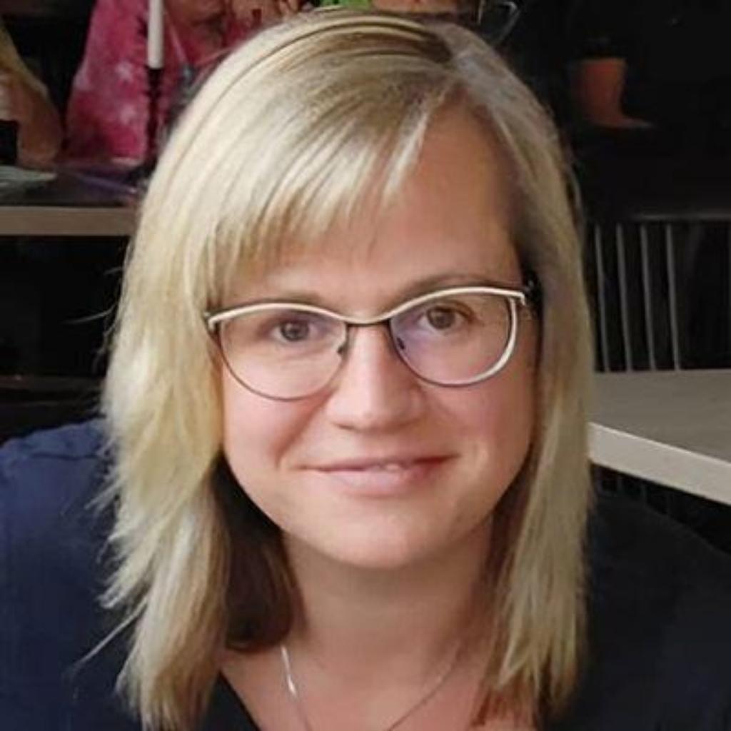Porträt von Mandy Hartung: Freundlich lächelnde Person mit blondem, schulterlangem Haar und Brille, aufgenommen in einem Innenraum